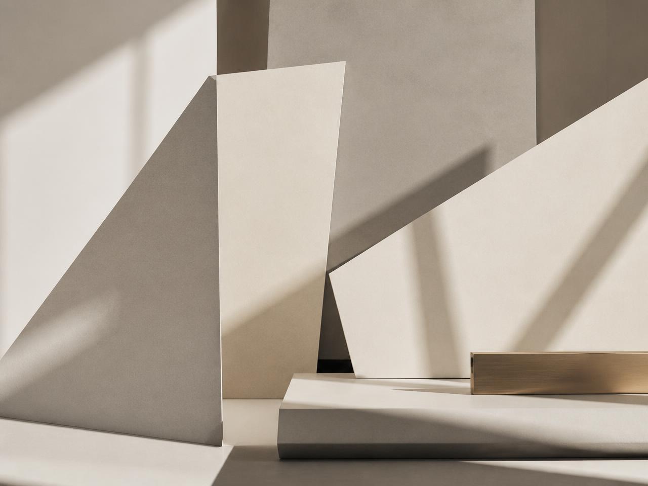 Ivory and grey paper planes arranged in overlapping geometric forms under directional daylight with a brass bar detail